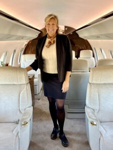 A professional woman stands confidently inside a luxurious private jet, wearing a blazer and scarf, showcasing the elegant interior.